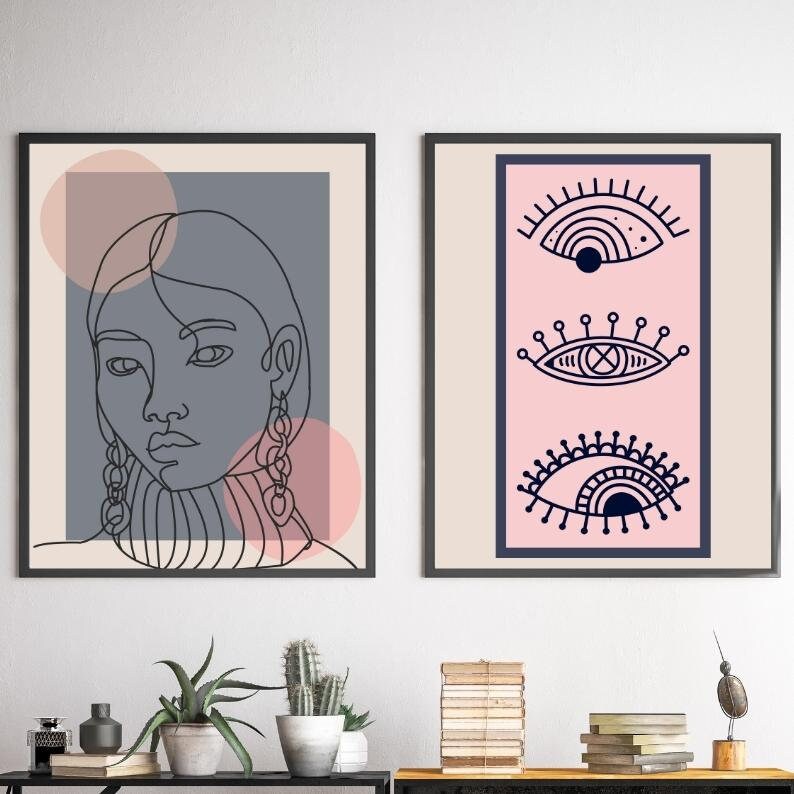 May include: Two framed prints, one with a line drawing of a woman's face and the other with three stylized eyes in navy blue on a pink background.