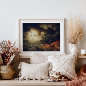 Op de afbeelding: Een ingelijst schilderij toont een stormachtige zeegezicht met donkere wolken en woelige golven. Het kunstwerk gebruikt een donker kleurenpalet met oranje en gele accenten, wat een dramatisch effect cre&euml;ert. Het schilderij wordt tentoongesteld boven decoratieve kussens en droge bloemstukken.