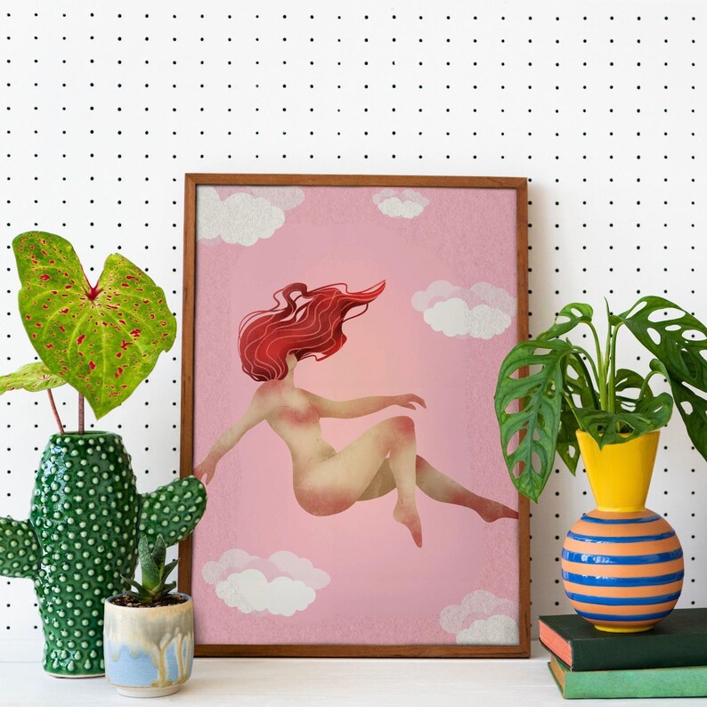 May include: A framed art print featuring a nude figure with flowing red hair floating in a pink sky with white clouds. The artwork is in a wooden frame and is displayed with potted plants in decorative vases.