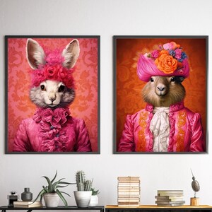 May include: Two framed prints of animal portraits. The first print features a rabbit wearing a pink and white ruffled dress and a pink flower crown. The second print features a marmot wearing a pink and gold ruffled dress and a pink turban with flowers.