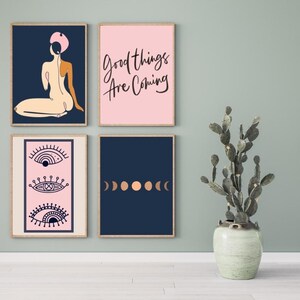 May include: Four framed prints with different designs. The top left print features a pink and blue illustration of a woman. The top right print is pink with the text "Good things are coming". The bottom left print is pink with three stylized eyes. The bottom right print is navy blue with five copper colored circles.