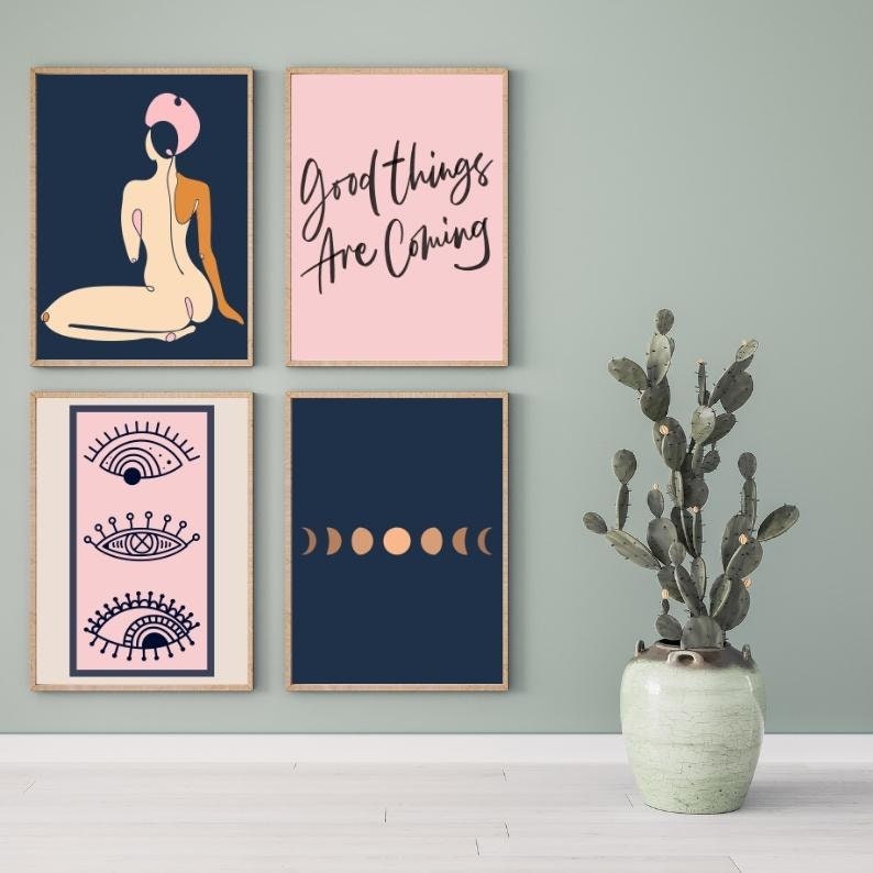 May include: Four framed prints with different designs. The top left print features a pink and blue illustration of a woman. The top right print is pink with the text "Good things are coming". The bottom left print is pink with three stylized eyes. The bottom right print is navy blue with five copper colored circles.