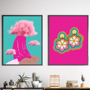 May include: Two framed art prints. One features a figure with a pink cloud for a head, set against a teal background. The other showcases flower-shaped earrings with smiley faces on a bright pink backdrop.