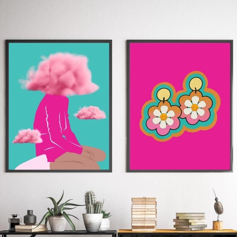 May include: Two framed art prints. One features a figure with a pink cloud for a head, set against a teal background. The other showcases flower-shaped earrings with smiley faces on a bright pink backdrop.