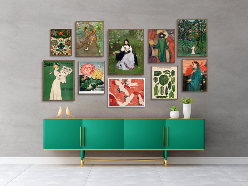 May include: A green dresser with gold accents and a collection of framed vintage prints featuring botanical illustrations, a woman reading a newspaper, and a woman in a garden. The prints are arranged on a gray wall above the dresser.