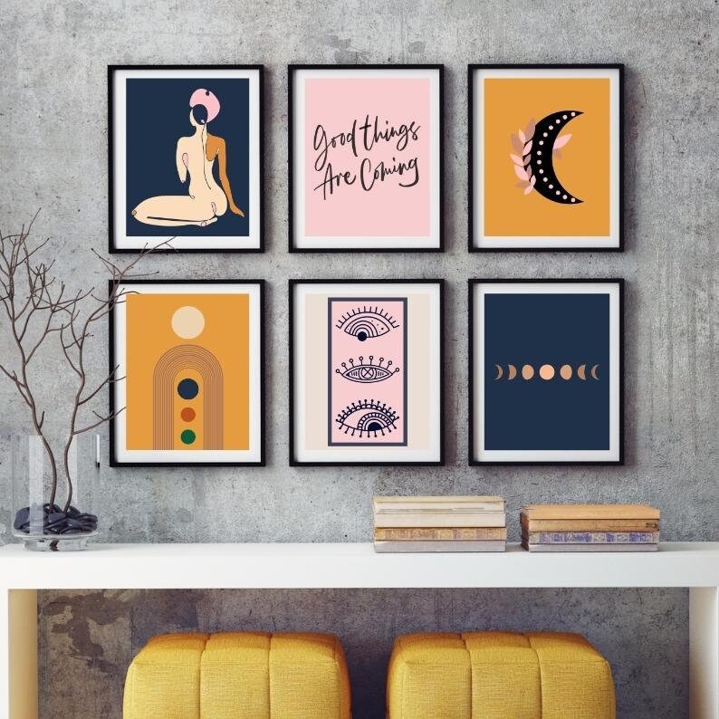 May include: Six black framed prints with various abstract designs. The prints feature a woman in a pink hat, a moon with a branch, a rainbow arch, three eyes, and a row of moons. The text "Good things are coming" is on one of the prints.