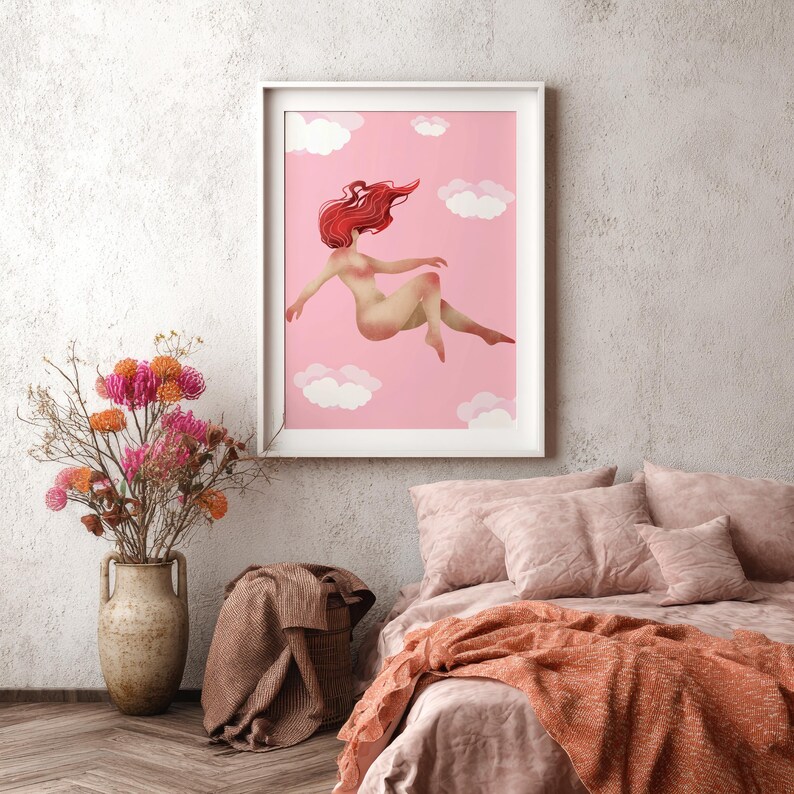 May include: A framed art print featuring a nude figure with flowing red hair floating among white clouds on a pink background. The artwork is displayed above a bed with pink bedding and an orange throw. A vase of flowers sits nearby.