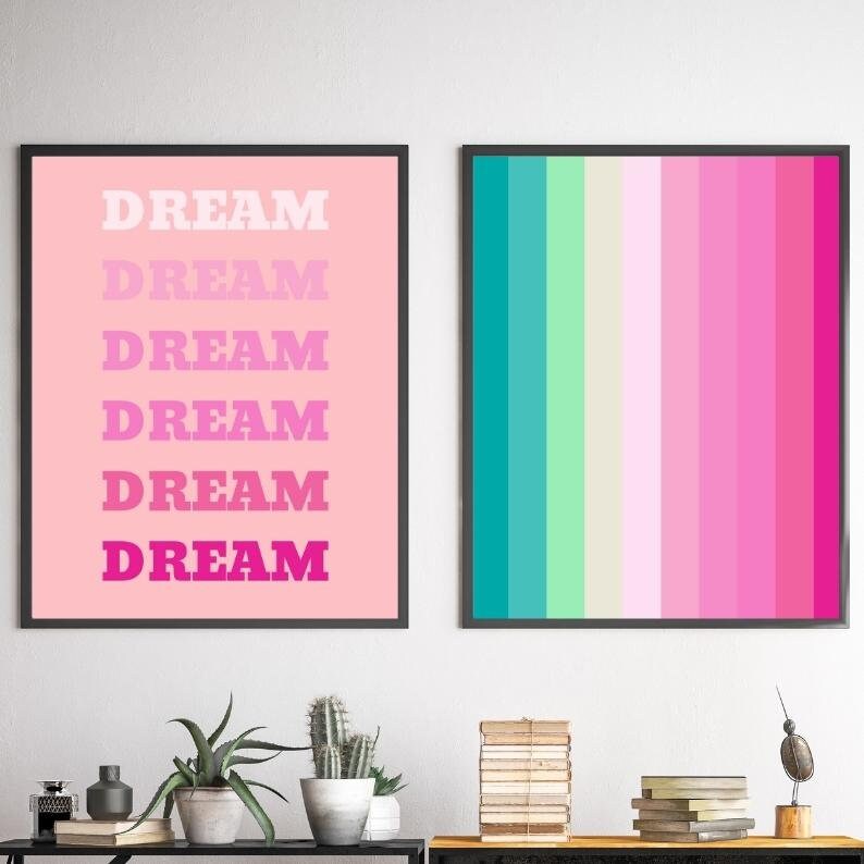 May include: Two framed art prints. One features the word "DREAM" in a gradient of pink hues against a pink background. The other print displays vertical stripes in shades of teal, green, pink, and magenta.