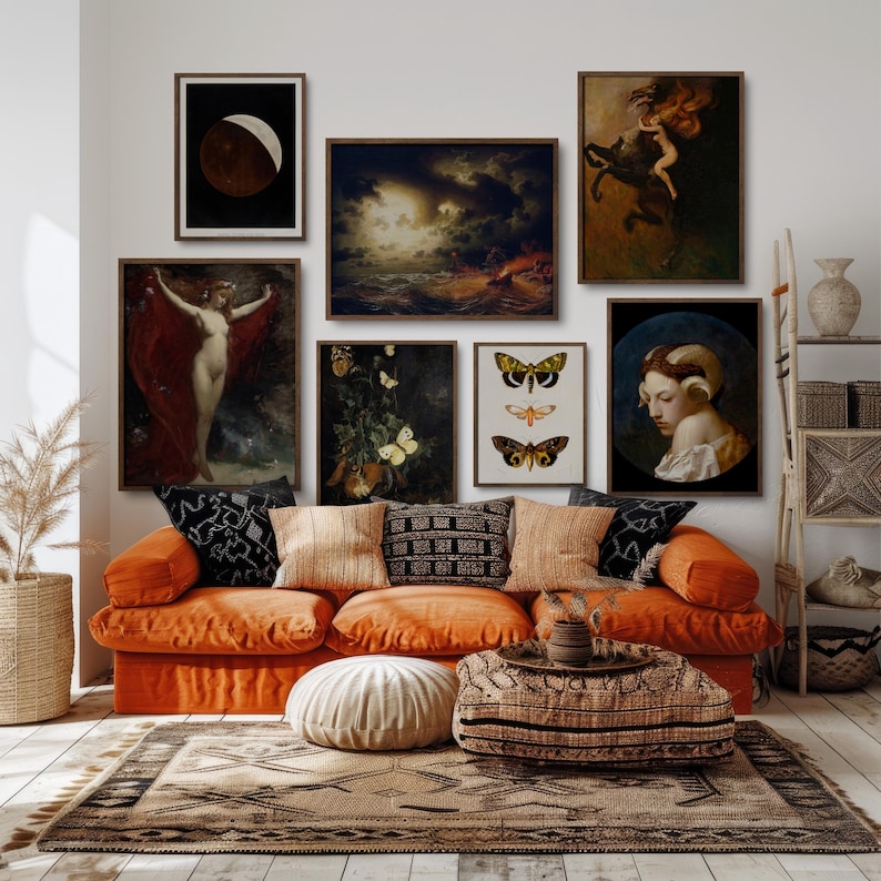 Op de afbeelding: Een eclectische woonkamer met een oranje bank versierd met kussens met patronen. Boven de bank een galerijmuur met ingelijste kunstdrukken, waaronder een maanfase en klassieke schilderijen. Een geweven vloerkleed en decoratieve ladder maken de bohemien esthetiek compleet.
