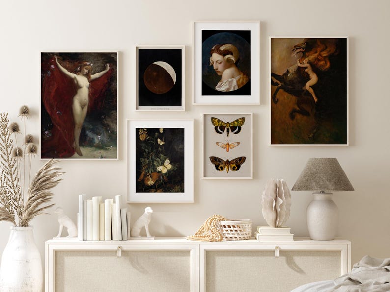 Op de afbeelding: Een galerijmuur met ingelijste kunstdrukken. De collectie omvat klassieke schilderijen van een naakte figuur met een rode draperie, een halve maan, een vrouw met ramshorens, een figuur op een paard en illustraties van vlinders en motten. Een lamp en decoratieve items staan op een witte kast.