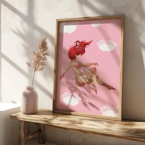 May include: A framed art print featuring a woman with flowing red hair floating among white clouds on a pink background. The artwork is in a wooden frame and is displayed on a wooden bench.