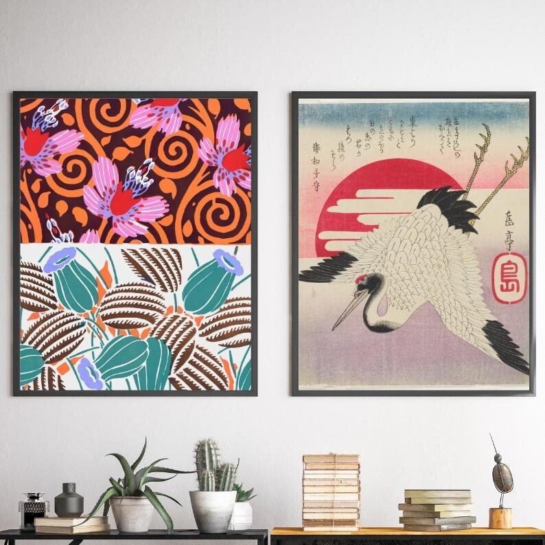 May include: Two framed prints featuring Japanese art. The print on the left has a floral pattern in shades of pink, orange, and brown. The print on the right depicts a white crane flying in front of a red sun with Japanese text.