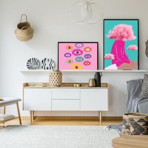 May include: A modern living room featuring two framed art prints. One print displays colorful eye illustrations on a pink background. The other depicts a figure with a pink cloud for a head. Decorative items include a woven basket, plates, and a white cabinet.