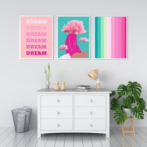 May include: Three framed art prints. The left print has the word "DREAM" stacked in pink and fuchsia. The center print features a figure with a pink cloud head. The right print has vertical stripes in shades of pink and green.