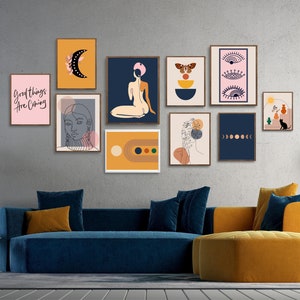 May include: A living room with a blue velvet sofa and a round ottoman. The wall behind the sofa is decorated with a gallery wall of framed prints featuring abstract designs, line art, and text. The prints are in various colors, including pink, blue, yellow, and orange. The text on one of the prints reads "Good things are coming."