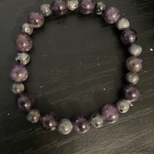 Könnte beinhalten: Ein violettes und graues Perlenarmband mit abwechselnden runden Perlen.