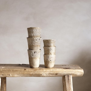 May include: A set of three ceramic mugs with a speckled, matte finish in cream, light brown, and dark brown. Each mug has a simple, minimalist design, ideal for tea or coffee.