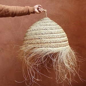 May include: A large, round, natural woven pendant light with a fringe of long, thin strands. The light is made of a light brown material and has a natural, rustic look.