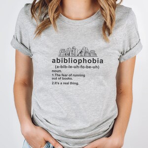 Pu&ograve; includere: Maglietta grigio chiaro con la parola "abibliophobia" stampata in nero, insieme alla sua pronuncia e definizione. La definizione recita: "La paura di rimanere senza libri. &Egrave; una cosa reale."