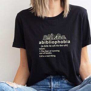 Pu&ograve; includere: T-shirt nera con la parola "abibliophobia" e la sua pronuncia tra parentesi. Sotto, viene data la definizione della parola: "La paura di rimanere senza libri. &Egrave; una cosa reale."
