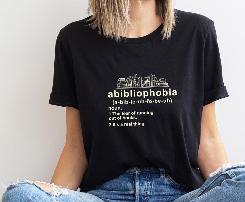 Pu&ograve; includere: T-shirt nera con la parola "abibliophobia" e la sua pronuncia tra parentesi. Sotto, viene data la definizione della parola: "La paura di rimanere senza libri. &Egrave; una cosa reale."