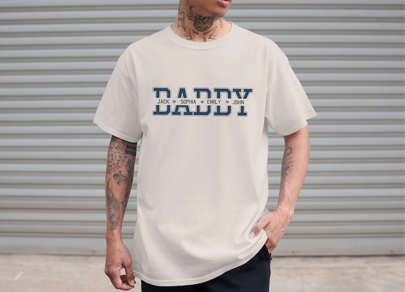 May include: A white t-shirt with a navy blue graphic that says "Daddy" with the names "Jack", "Sophia", "Emily", and "John" underneath.