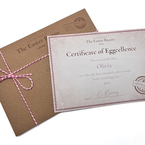 May include: A brown envelope with a pink and white twine bow, tied around it. The envelope is addressed to "The Easter Bunny". A certificate of eggcellence is on top of the envelope. The certificate is printed on white paper with a pink border. The certificate states "This is to certify that Olivia has officially been awarded a place on the Easter Good Egg List 2023. Signed E. Bunny. Approved."