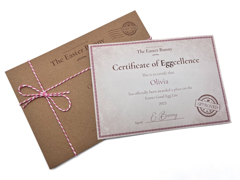 May include: A brown envelope with a pink and white twine bow, tied around it. The envelope is addressed to "The Easter Bunny". A certificate of eggcellence is on top of the envelope. The certificate is printed on white paper with a pink border. The certificate states "This is to certify that Olivia has officially been awarded a place on the Easter Good Egg List 2023. Signed E. Bunny. Approved."