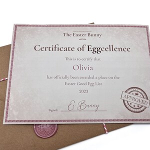 May include: A certificate of Eggcellence, signed by the Easter Bunny, is awarded to Olivia for being on the Easter Good Egg List in 2023. The certificate has a pink border and a red wax seal.