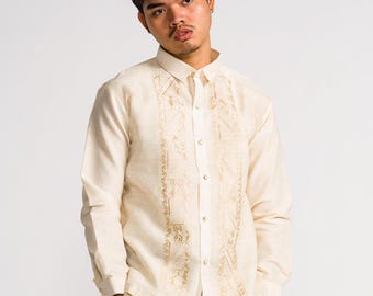 May include: A long-sleeved, cream-colored button-down shirt featuring a vertical panel of intricate, tonal embroidery along the front placket, paired with matching cream-colored trousers. The shirt has a structured collar and buttoned cuffs.