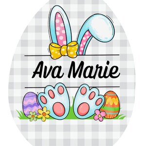 May include: A light blue Easter egg with a white and pink bunny peeking out. The bunny has a yellow bow and blue paw prints. The egg has a gray and white checkered background and the name "Ava Marie" written on it.