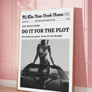 May include: A framed black and white print of a newspaper front page. The headline reads "DO IT FOR THE PLOT." The image features a woman in a bikini on a car. The newspaper is titled "The New York News."