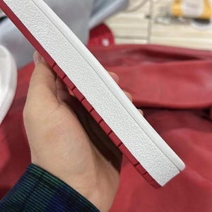 May include: A white and red shoe sole with a textured white upper and a red bottom. The sole is held in a hand, showcasing the design and materials. The shoe sole is likely for a sneaker or athletic shoe.