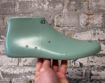 Könnte beinhalten: Eine hellgrüne Schuhform mit der Nummer 43 darauf gedruckt. Die Form besteht aus einem strukturierten Material und hat eine abgerundete Spitze.