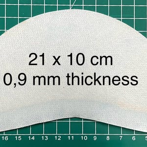 Puede incluir: Una pieza de material blanca en forma de media luna que mide 21 cm por 10 cm y 0,9 mm de grosor.