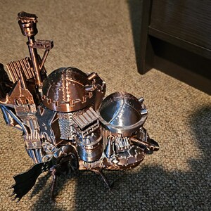 Op de afbeelding: Een 3D-geprint model van een steampunk-achtige vliegmachine met ingewikkelde details en een koperen afwerking. Het model heeft meerdere koepels en torens, en een lange, gebogen vleugel.