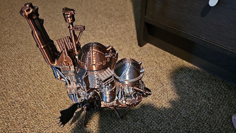 Op de afbeelding: Een 3D-geprint model van een steampunk-achtige vliegmachine met ingewikkelde details en een koperen afwerking. Het model heeft meerdere koepels en torens, en een lange, gebogen vleugel.