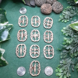 May include: Twelve wooden oval-shaped pieces with intricate cut-out designs. The pieces are arranged in three rows of four, with the top row slightly offset. The pieces are a light brown color and have a smooth, polished finish.