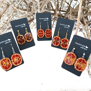 May include: Four pairs of earrings made from natural materials, each pair displayed on a black card with the text "Handmade with love". The earrings are made from a reddish-brown material with a natural pattern.