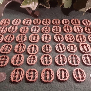 May include: A collection of 40 brown wooden carved buttons with a decorative design. The buttons are arranged in rows on a brown surface.