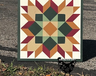 May include: A square wooden barn quilt featuring a geometric star pattern in shades of dark green, light green, burgundy, and tan on a white background. The text BARN QUILTS BY KARLY is printed in white near the bottom right corner of the board.