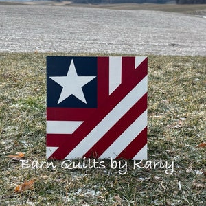 May include: A square wooden barn quilt featuring the American flag design. The quilt has a blue square with a white star in the upper left corner, with red and white stripes. The text "Barn Quilts by Karly" is at the bottom.