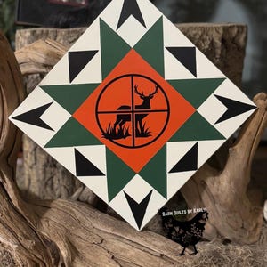 May include: A white, green, and orange barn quilt with a black silhouette of a deer in a target circle. The quilt is in a diamond shape and has a black and white star pattern. The text "BARN QUILTS BY KARLY" is in the bottom right corner.