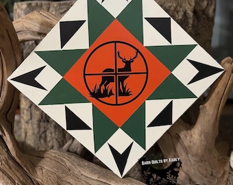 May include: A white, green, and orange barn quilt with a black silhouette of a deer in a target circle. The quilt is in a diamond shape and has a black and white star pattern. The text "BARN QUILTS BY KARLY" is in the bottom right corner.