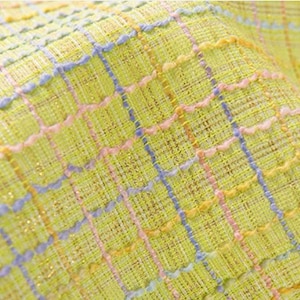 Puede incluir: Primer plano de una tela amarilla con un patrón de cuadros tejidos en hilos rosa, azul y amarillo. La tela tiene un brillo sutil.