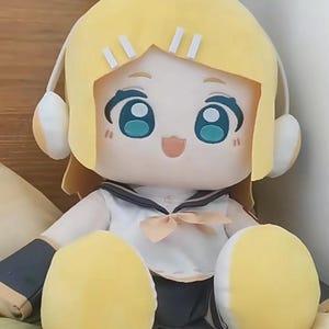 May include: A plush doll featuring a cartoon character with yellow hair and large teal eyes. The doll wears a sailor-style outfit with a bow and headphones. The doll's arms and legs are yellow.