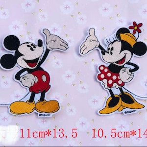 May include: Two embroidered iron-on patches featuring Mickey Mouse and Minnie Mouse. Mickey is wearing red shorts and yellow shoes. Minnie is wearing a red and white polka dot dress and yellow shoes. Both patches have the Disney logo.