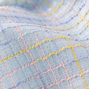 May include: A light blue fabric with a checkered pattern. The fabric is woven with pink, yellow, and purple threads.