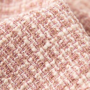 Può includere: Primo piano di un tessuto tweed rosa e bianco con un leggero luccichio. Il tessuto ha una trama tessuta e una sensazione morbida e lussuosa.