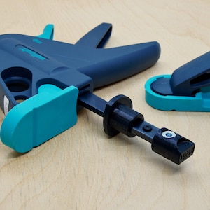 May include: A blue and teal clamp with a black handle and a teal and black foot pedal. The clamp is made of plastic and has a metal screw. The foot pedal is used to tighten the clamp.